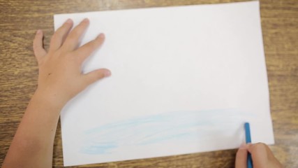 Girl draws with blue chalk for drawing makes an artistic drawing of the ocean or sea on a white sheet. Hand of a girl with a chalk for drawing close-up. Child's drawing