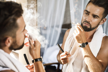 Man looking in the mirror, smoking a cigarette and shaving his beard with a straight razor