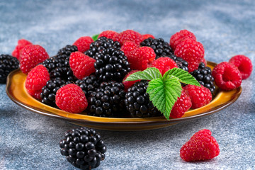 raspberries and blackberries in a plate on a blue background