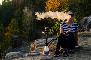 A woman smoking shisha (hookah) sitting by the sea. Seagulls at the background.