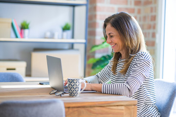 Middle age senior woman sitting at the table at home working using computer laptop with a happy face standing and smiling with a confident smile showing teeth