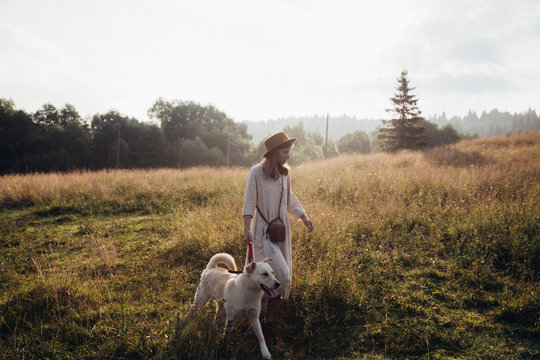 Beautiful young woman relaxed and carefree enjoying a summer sunset with her lovely dog on the straw field background