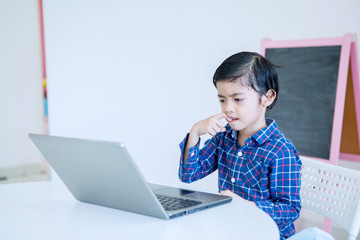 Little boy thinking something during using a laptop