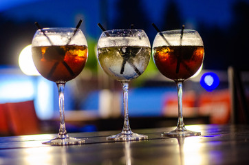 Beautiful row line of different colored alcohol cocktails on a party, martini, vodka,and others on decorated catering bouquet table on open air event, picture with beautiful bokeh