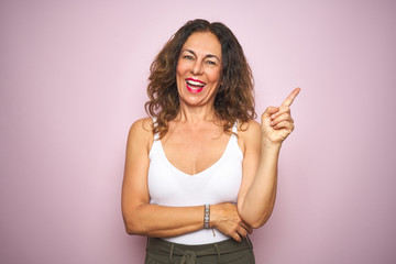 Middle age senior woman standing over pink isolated background with a big smile on face, pointing with hand and finger to the side looking at the camera.