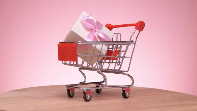 Shopping cart with gift rotates on a pink background