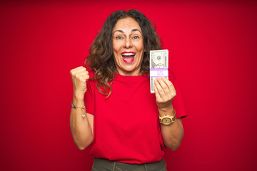 Middle age senior woman holding bunch of dollars over red isolated background screaming proud and...