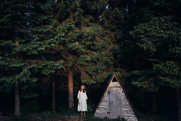 Woman pretty wear amazing white dress and hat on forest and wooden wigwam background . Perfect plase for ceremony. © gartmanart