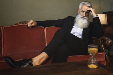 Handsome bearded senior man is looking at hourglass