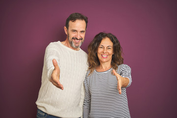 Obraz premium Beautiful middle age couple wearing winter sweater over isolated purple background smiling friendly offering handshake as greeting and welcoming. Successful business.