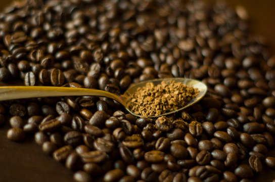 Instant granulated coffee in the spoon at the background of aromatic coffee beans, close-up image with a copyspace for a text