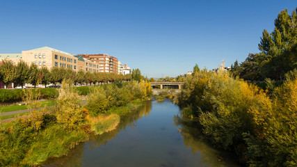 Fototapeta na wymiar Bernesga River in autumn as it passes through the city of León with green areas, shrubs and groves on the banks. Spain