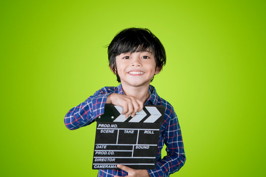 Smiling little boy holds a clapperboard on studio