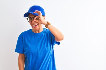 Senior deliverywoman wearing cap and glasses standing over isolated white background doing ok gesture with hand smiling, eye looking through fingers with happy face.