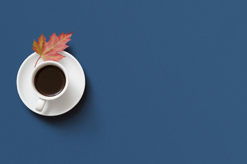 Autumn coffee cup with coloured maple feaf on dark blue background, Flat Lay with Copy Space