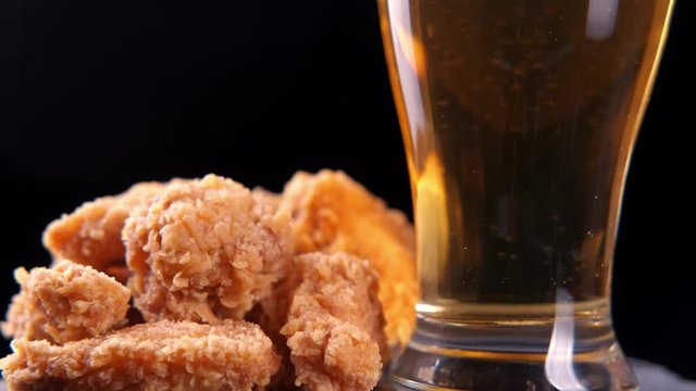 Grilled chicken wings and a glass of beer on black. 4K rotation