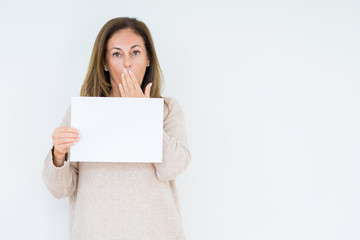 Fototapeta premium Middle age woman holding blank paper sheet over isolated background cover mouth with hand shocked with shame for mistake, expression of fear, scared in silence, secret concept