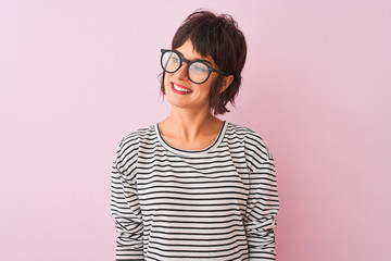 Young beautiful woman wearing striped t-shirt and glasses over isolated pink background looking...