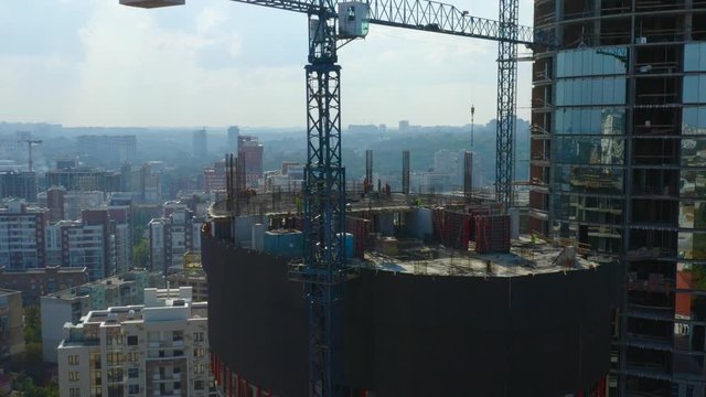 Aerial circling view of the modern office skyscraper under construction (in a course of building) with a lot of workers on the rooftop in the big city on a sunny day