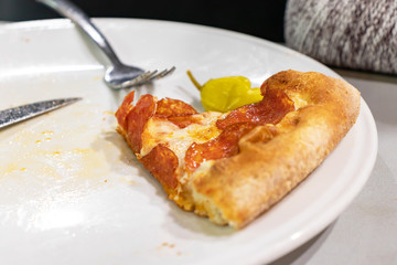 A slice of pepperoni pizza on white plate with folk and knife on a table of italian restaurant