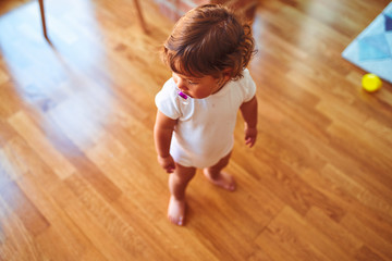 Beautiful toddler child girl wearing white t-shirt standing on the floor using pacifier
