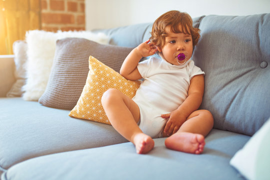 Beautiful toddler child girl wearing white t-shirt sitting on the sofa using pacifier