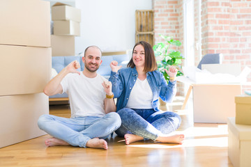 Young couple sitting on the floor arround cardboard boxes moving to a new house looking confident with smile on face, pointing oneself with fingers proud and happy.