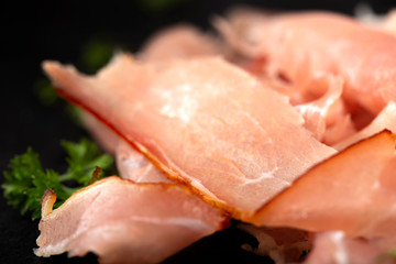 Thin sliced smoked pork ham on a dark slate with herbs