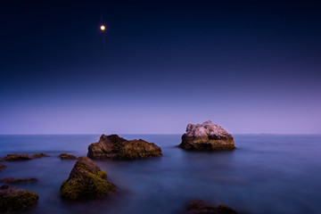 night sea landscape with rocks in the foreground and full moon