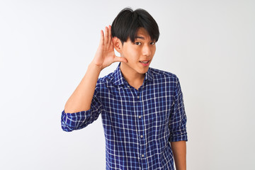 Young chinese man wearing casual blue shirt standing over isolated white background smiling with hand over ear listening an hearing to rumor or gossip. Deafness concept.