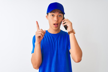 Chinese deliveryman wearing cap talking on the smartphone over isolated white background surprised with an idea or question pointing finger with happy face, number one