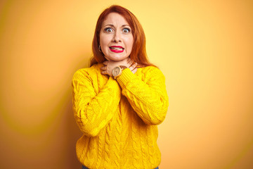 Beautiful redhead woman wearing winter sweater standing over isolated yellow background shouting suffocate because painful strangle. Health problem. Asphyxiate and suicide concept.