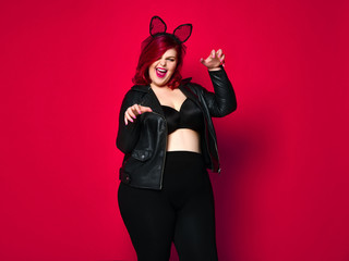 Cute sexy plus size brunette with black bunny ears in leather jacket and underwear posing on red background