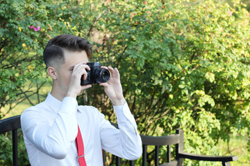 Fototapeta na wymiar Stylishly dressed young man sits taking pictures in the park. In his hands holds a SLR film camera.