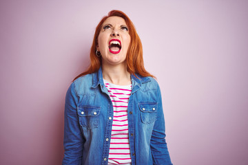 Beautiful redhead woman wearing denim shirt and striped t-shirt over isolated pink background angry and mad screaming frustrated and furious, shouting with anger. Rage and aggressive concept.