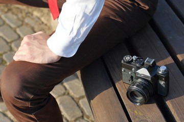 Stylishly dressed young man sits on a park bench. Nearby lies a SLR film camera.