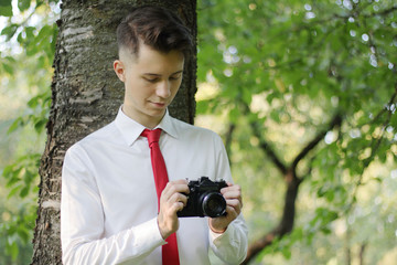 Stylishly dressed young man posing in a park. Holds the camera in his hands and works with the...
