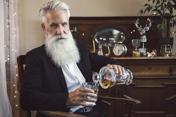 Handsome bearded senior man pouring whiskey into the glass