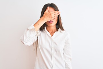 Young beautiful businesswoman wearing glasses standing over isolated white background covering eyes with hand, looking serious and sad. Sightless, hiding and rejection concept