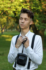 Stylishly dressed young man posing in a park. Laughing brings his hands to his chest. In the hands of the camera in a case.