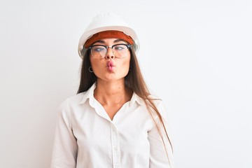 Young beautiful architect woman wearing helmet and glasses over isolated white background making fish face with lips, crazy and comical gesture. Funny expression.