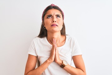 Young beautiful woman wearing casual t-shirt and diadem over isolated white background begging and...