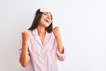 Young beautiful woman wearing sleep mask and pajama over isolated white background celebrating surprised and amazed for success with arms raised and eyes closed. Winner concept.