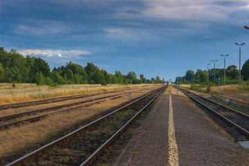 Fototapeta na wymiar Railway station train in the distance near stands approaching perspective tracks reflections nature evening blue sky transport of people mood small town