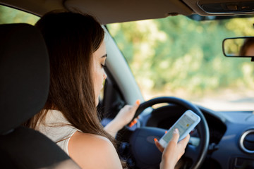 Fototapeta na wymiar Young female student texting writing messages while driwing a car and doesn`t control the situation. Dangerous driving, addiction to socil medias