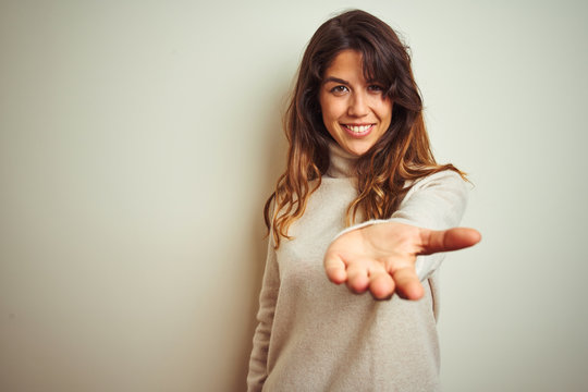 Young beautiful woman wearing winter sweater standing over white isolated background smiling cheerful offering palm hand giving assistance and acceptance.