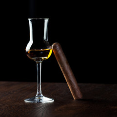 Tall glass of cognac with the Cuban cigar on black background