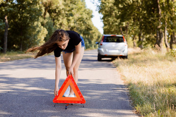 Student girl placing red emergency red stop sign near the broken car on the road