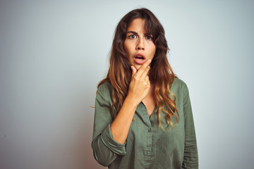 Young beautiful woman wearing green shirt standing over grey isolated background Looking fascinated with disbelief, surprise and amazed expression with hands on chin