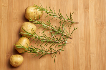 Rosemary with raw Potatoes on wooden background bamboo